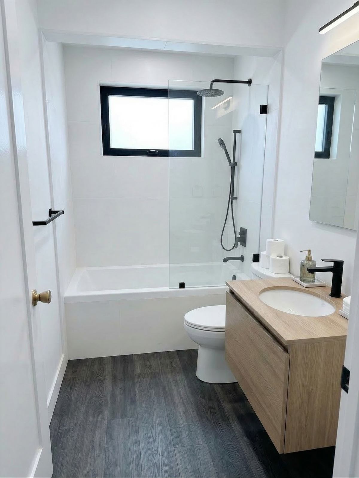Remodeled bathroom with glass shower panel and floating wood vanity